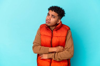 Genç Afro-Amerikalı kıvırcık adam mavi üzerine izole edilmiş, şüpheli, belirsiz, seni inceliyor..