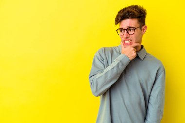 Kafkasyalı genç adam sarı arka planda izole edilmiş kafasının arkasına dokunuyor, düşünüyor ve bir seçim yapıyor..