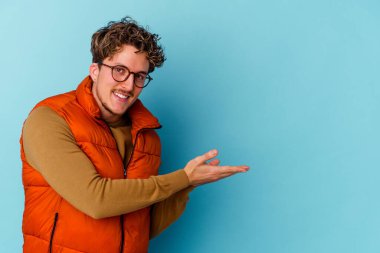 Mavi arka planda izole edilmiş gözlük takan genç beyaz bir adam palmiye ağacında bir fotokopi alanı tutuyor..