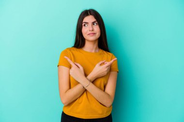 Mavi arka plan noktalarında izole edilmiş genç beyaz kadın iki seçenek arasında seçim yapmaya çalışıyor..