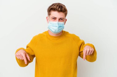 Koronavirüs maskesi takan genç adam beyaz arka planda izole edilmiş, parmakları aşağıda, olumlu bir his var..