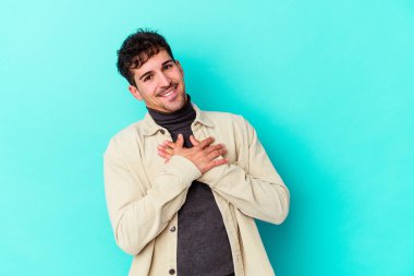 Mavi arka planda izole edilmiş beyaz bir genç, dost bir ifadeye sahip, avuçlarını göğsüne bastırıyor. Aşk konsepti.