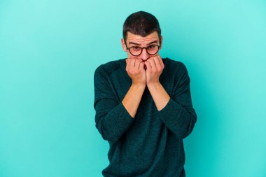 Mavi arka planda izole edilmiş, tırnak yiyen, gergin ve endişeli genç bir beyaz adam..