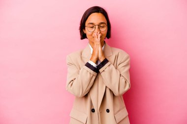 Genç iş kadını, pembe arka planda izole edilmiş, el ele tutuşmuş, ağız kenarında dua eden, kendinden emin..