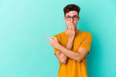 Mavi arka planda izole edilmiş genç beyaz adam yan tarafı işaret ediyor.