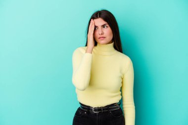 Kafkasyalı genç bir kadın mavi arka planda izole edilmiş, başı ağrıyor, yüzüne dokunuyor..