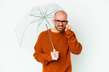 Şemsiyesi olan kel bir genç adam elleriyle kulaklarını kapatıyor..