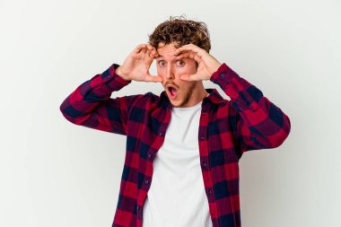 Beyaz arka planda izole edilmiş genç beyaz bir adam bir başarı fırsatı bulmak için gözlerini açık tutuyor..