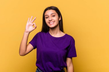 Sarı arka planda izole edilmiş genç Hintli kadın neşeli ve kendinden emin, iyi bir hareket gösteriyor..