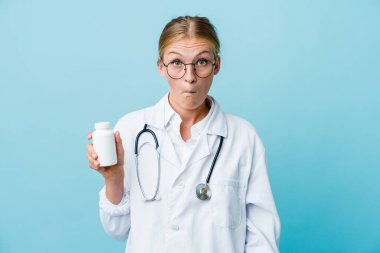 Genç Rus doktor elinde ilaç şişesi, mavi omuz silkiyor ve gözleri açık..