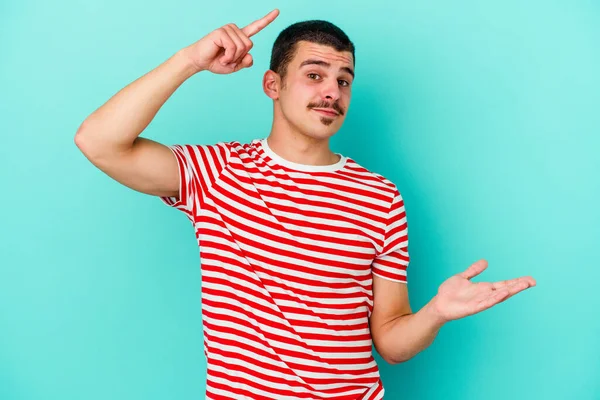 Kafkasyalı genç adam mavi arka planda izole edilmiş ve elinde bir ürün tutuyor..