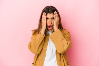 Pembe arka planda izole edilmiş genç Hintli kadın yüzünün yarısını avuç içiyle kaplayarak eğleniyor..