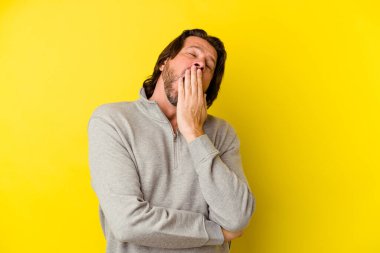 Orta yaşlı beyaz bir adam sarı arka planda izole edilmiş. Esniyor. Ağzı eliyle kapatan yorgun bir hareket sergiliyor..