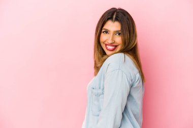 Pembe arka planda soyutlanmış genç Hintli kadın gülümseyen, neşeli ve keyifli bir kenara bakıyor..