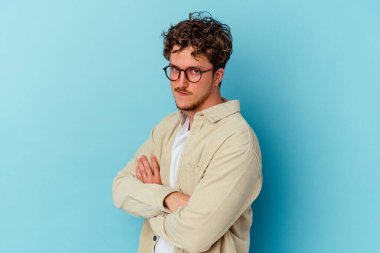 Mavi arka planda izole edilmiş gözlük takan genç beyaz adam amaçlarına ve amaçlarına ulaşma hayali kuruyor.