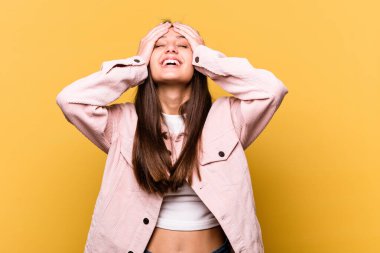 Sarı arka planda izole edilmiş genç Hintli kadın mutlu bir şekilde ellerini başının üstünde tutarak gülüyor. Mutluluk kavramı.