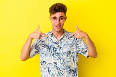 Sarı arka planda izole edilmiş genç beyaz adam parmağını göstererek şaşırdı ve gülümsedi..