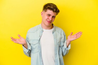 Sarı arka planda izole edilmiş genç beyaz adam sorgulama sırasında omuz silkiyor ve kuşkulanıyor..