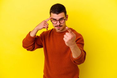 Sarı arka planda izole edilmiş genç beyaz adam şakağı parmağıyla işaret ediyor, düşünüyor ve bir göreve odaklanıyor..