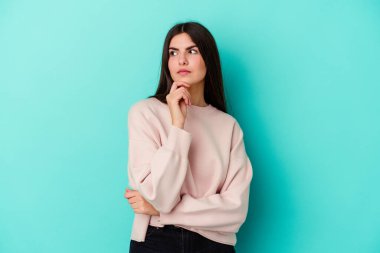 Kafkasyalı genç bir kadın mavi arka planda izole edilmiş şüpheli, belirsiz, seni muayene ediyor..