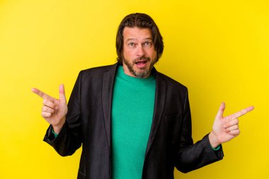 Sarı arka planda izole edilmiş orta yaşlı beyaz bir adam farklı kopya alanlarını gösteriyor, birini seçiyor, parmağıyla gösteriyor..