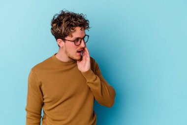 Mavi arka planda gözlüklü genç beyaz adam gizli bir sıcak fren haberi veriyor ve yan bakıyor.