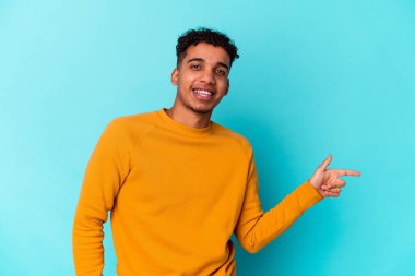 Genç Afro-Amerikalı kıvırcık adam mavi üzerine izole edilmiş, mutlu bir şekilde işaret parmağıyla işaret ediyor..