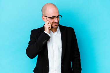 Genç, beyaz, kel bir adam mavi arka planda izole edilmiş kulakları elleriyle kapatıyor..