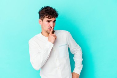 Mavi arka planda izole edilmiş genç beyaz bir adam ya sır saklıyor ya da sessizlik istiyor..