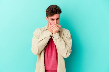 Kafkasyalı genç adam mavi arka planda izole edilmiş ağzı kapalı ve elleri endişeli görünüyor..