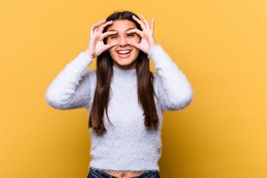 Sarı arka planda izole edilmiş genç Hintli kadın bir başarı fırsatı bulmak için gözlerini açık tutuyor..