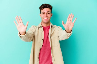 Mavi arka planda izole edilmiş genç beyaz adam on numarayı elleriyle gösteriyor..