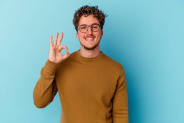 Gözlüklü genç beyaz adam mavi arka planda izole edilmiş neşeli ve kendinden emin..