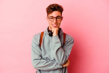 Genç bir öğrenci pembe arka planda izole edilmiş mutlu ve kendinden emin gülümsüyor, elleriyle çenesine dokunuyor..