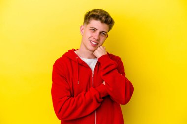 Sarı arka planda izole edilmiş genç, mutlu ve kendinden emin gülümseyen, elleriyle çenesine dokunan beyaz bir adam..