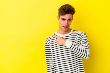 Sarı arka planda izole edilmiş genç beyaz adam gülümsüyor ve boş alanda bir şeyler gösteriyor..