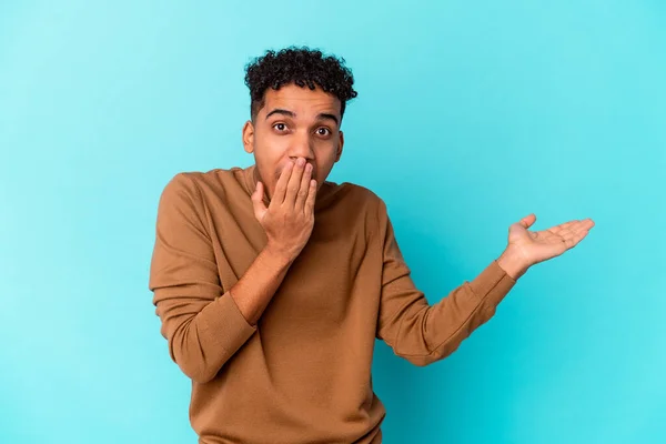 Jovem Afro Americano Encaracolado Homem Isolado Azul Impressionado Segurando Espaço — Fotografia de Stock