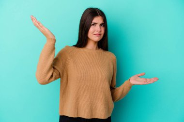 Kafkasyalı genç bir kadın mavi arka planda izole edilmiş. Kafası karışmış ve omuz silkiyor. Kopya alanını tutmak için..