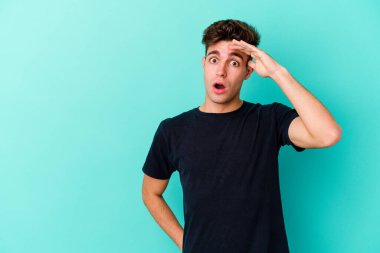 Mavi arka planda izole edilmiş genç beyaz adam yüksek sesle bağırıyor, gözleri açık ve elleri gergin tutuyor..