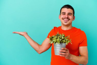 Mavi arka planda bir yaprak tutan genç beyaz bir adam avucunun içinde bir kopya alanı ve belinde başka bir el tutan.