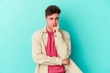 Kafkasyalı genç bir adam mavi arka planda izole edilmiş. Bir strateji planlıyor, bir iş yolu düşünüyor..