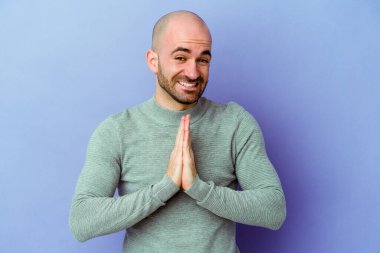 Mor arka planda izole edilmiş beyaz kel bir adam. Ağız kenarında el ele dua ediyor. Kendinden emin..