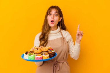 Sarı arka planda izole edilmiş genç pasta şefi kadının harika bir fikri var, yaratıcılık kavramı..