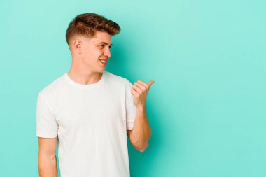 Kafkasyalı genç adam mavi arka plan noktalarında izole edilmiş başparmak uzakta, gülüyor ve kaygısız.