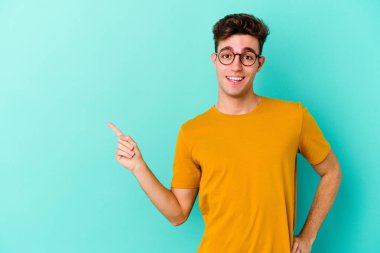 Mavi arka planda izole edilmiş genç beyaz adam işaret parmağıyla işaret ederek gülümsüyor..