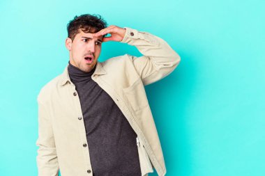 Kafkasyalı genç adam mavi arka planda izole edilmiş, uzaklara bakıyor ve elini alnına koyuyor..