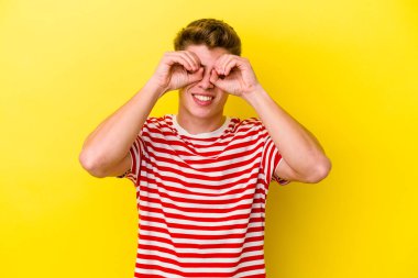 Sarı arka planda izole edilmiş genç beyaz adam gözlerinde sorun olmadığını gösteriyor.