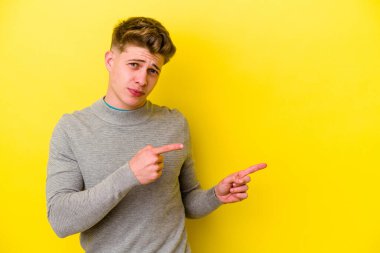 Sarı arka planda izole edilmiş genç beyaz adam işaret parmağıyla fotokopi alanını işaret ederek şok oldu..
