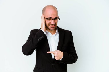 Genç, beyaz, kel bir adam mavi arka planda izole edilmiş bir şekilde bir dedikoduyu dinlemeye çalışıyor..