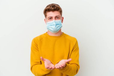 Coronavirus maskesi takan genç bir adam beyaz arka planda izole edilmiş, avuç içli bir şey tutuyor ve kameraya sunuyor..
